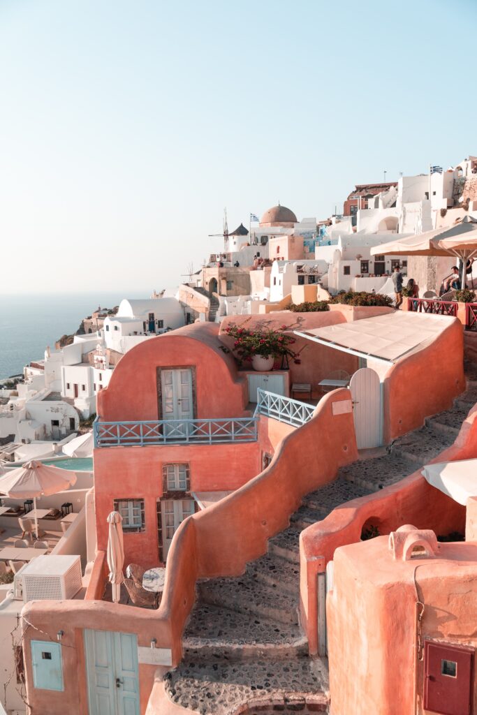 A breathtaking Santorini sunset over the iconic village of Oia, with whitewashed buildings perched on cliffs overlooking the caldera, as the sun sets, casting warm golden hues across the sky and sea.